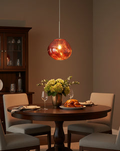 Copper pendant lit above a round dining table beside a dark glazed cabinet