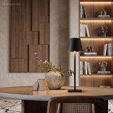 Black cordless lamp lighting a round dining table beside a styled shelf