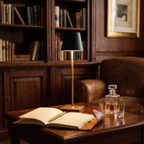 Cordless lamp lighting an open book and decanter on a dark desk