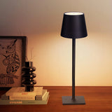 Black cordless lamp lit close up beside books and a dark vase