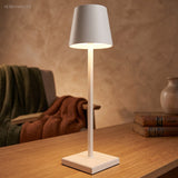 White cordless table lamp lighting a table beside a folded throw