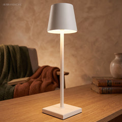 White cordless table lamp lighting a table beside a folded throw