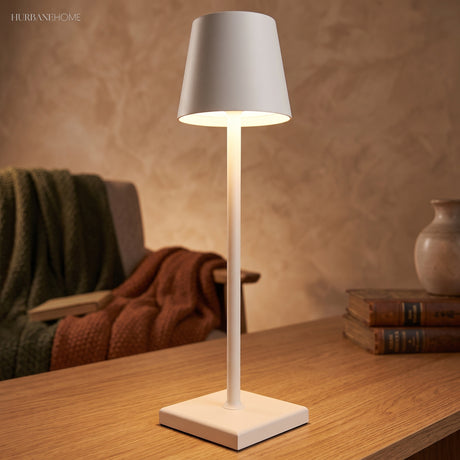 White cordless table lamp lighting a table beside a folded throw