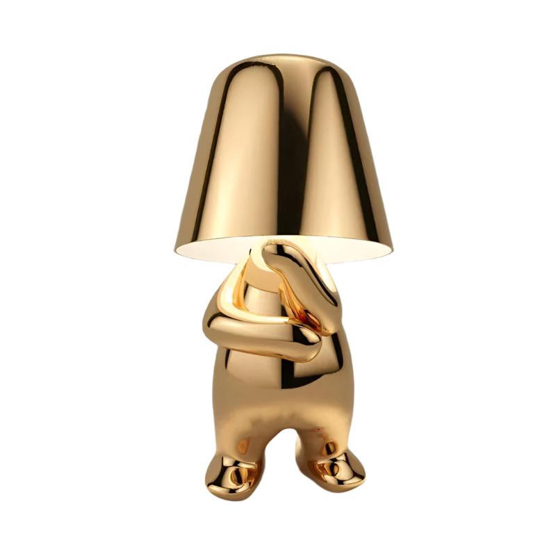 Gold figurine lamp standing with its arms folded across its chest