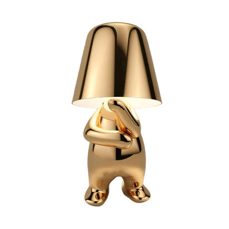 Gold figurine lamp standing with its arms folded across its chest
