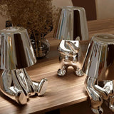 Three silver figurine lamps grouped on a wooden table top