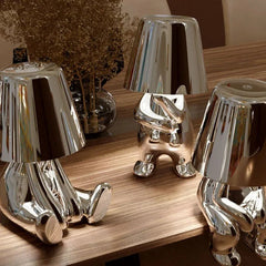 Three silver figurine lamps grouped on a wooden table top