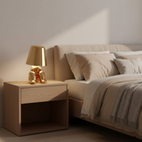 Gold figurine lamp lit on a bedside cabinet beside a made bed