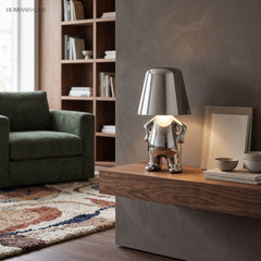 Silver figurine lamp lit on a wooden sideboard beside a green chair