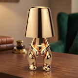 Gold figurine table lamp lit on a walnut desk beside books