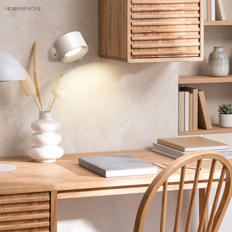 White cordless wall sconce above a wood desk casting a warm downward glow