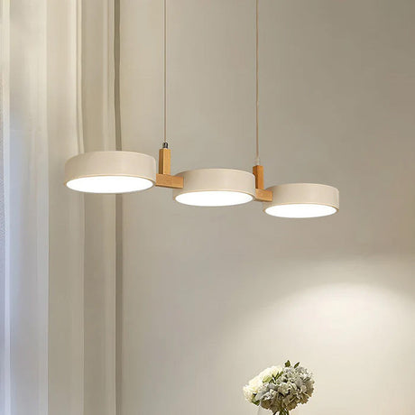 Three cream drum shades on a wood bar glowing against a soft grey wall