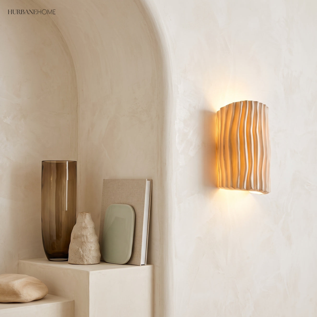 Cream resin wall sconce glowing on an arched plaster wall beside a vase
