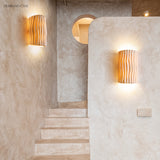 Two cream wall sconces lighting a plaster stairwell with a round window