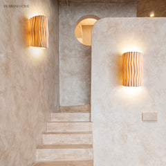 Two cream wall sconces lighting a plaster stairwell with a round window
