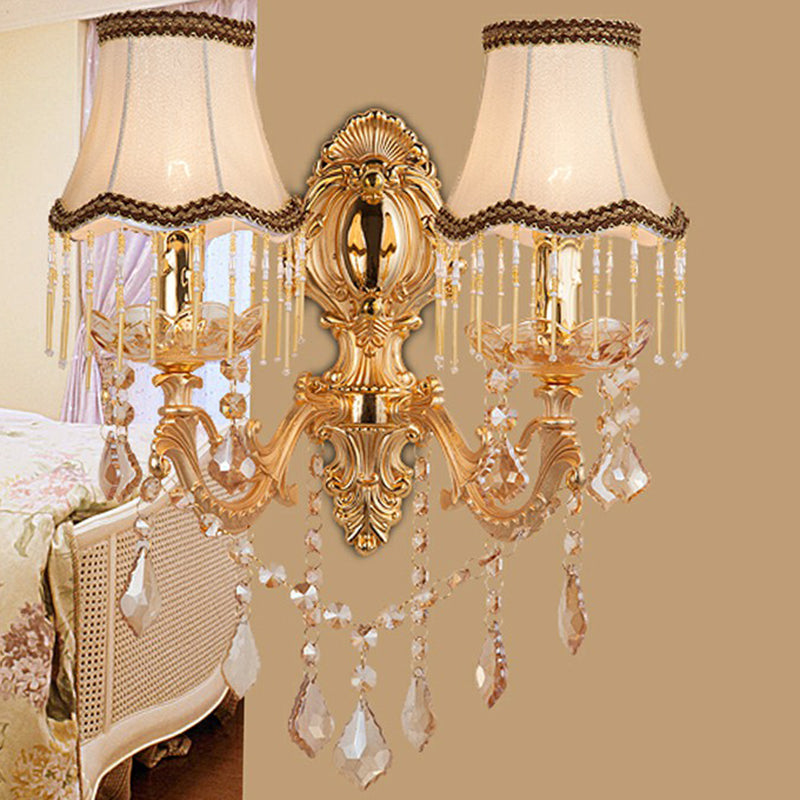 Gold sconce with fringed fabric shades and crystal drops in a bedroom