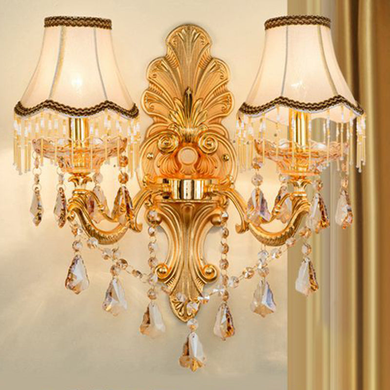 Gold crystal sconce with fabric shades against a draped gold curtain