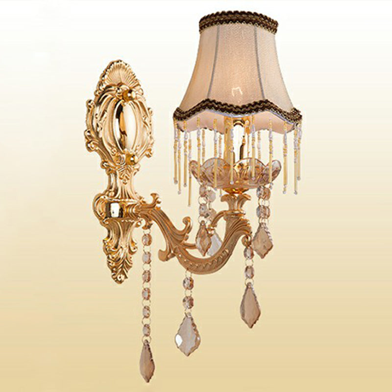 Single arm gold sconce with a fringed fabric shade and crystals