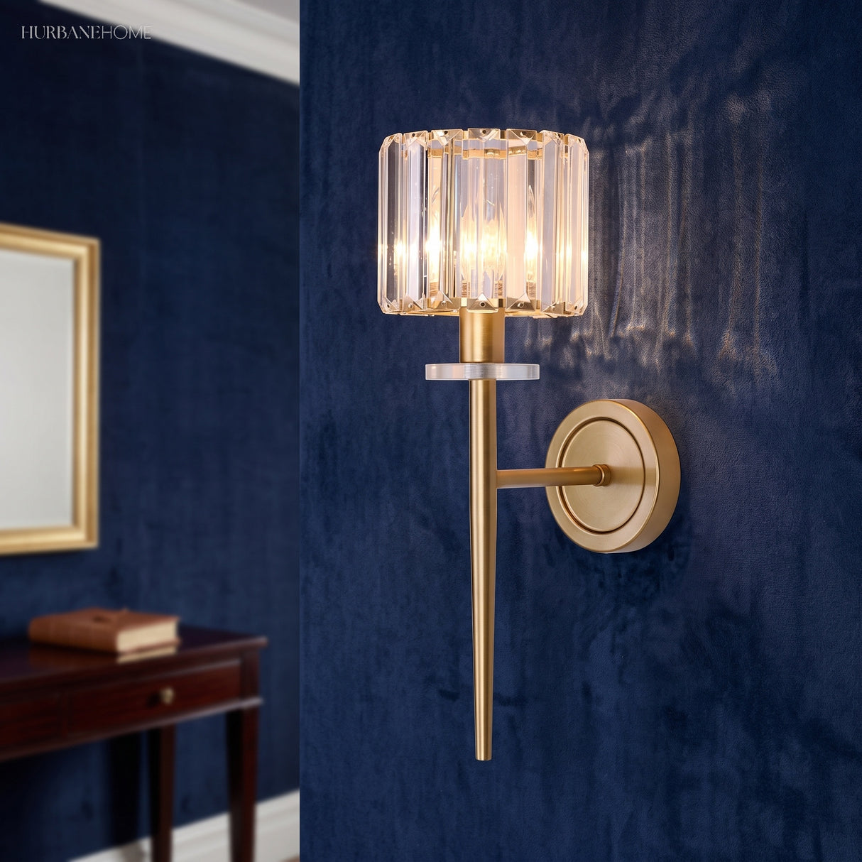 Gold crystal sconce lit on a blue wall above a dark console