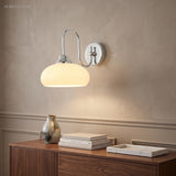 Chrome curved glass wall sconce above a walnut sideboard