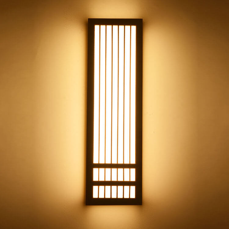 Tall dark walnut wall sconce lit against a warm painted wall