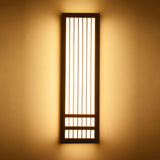 Tall dark walnut wall sconce lit against a warm painted wall