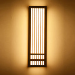 Tall dark walnut wall sconce lit against a warm painted wall
