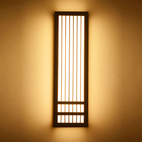 Tall dark walnut wall sconce lit against a warm painted wall