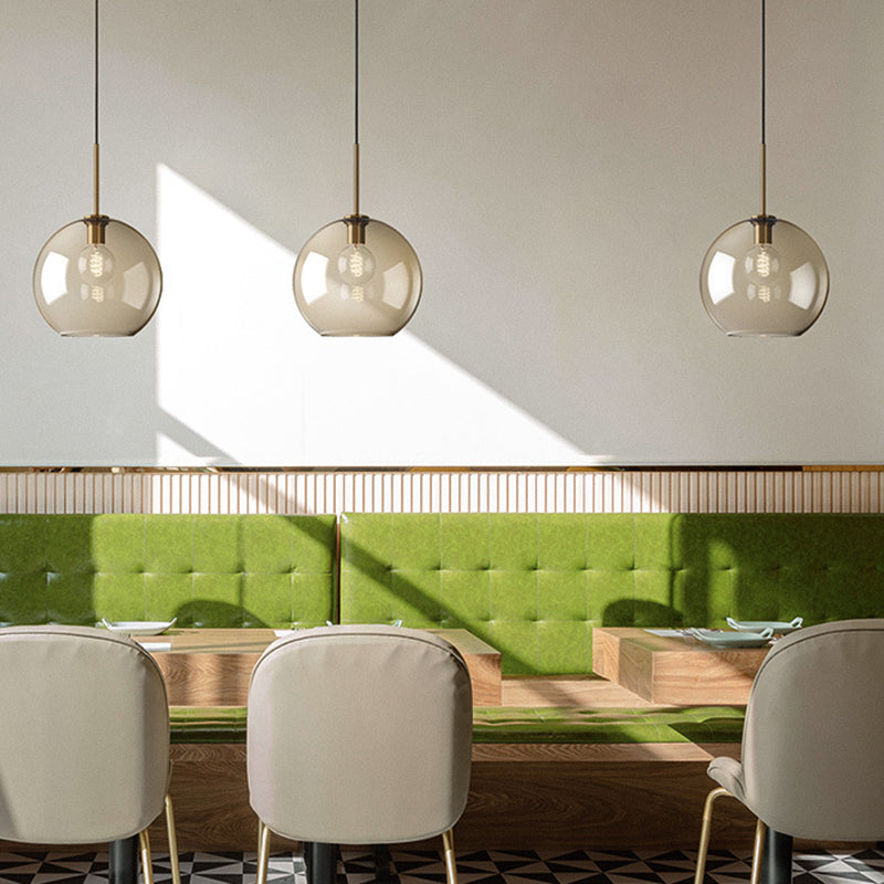 Three amber globe pendants over a dining table with green seating