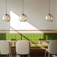Three amber globe pendants over a dining table with green seating