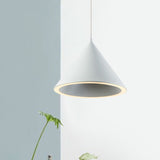 White cone pendant lit against a pale blue wall beside a plant