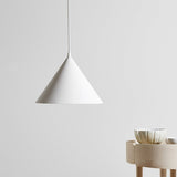 White cone pendant lit against a plain wall beside a sideboard