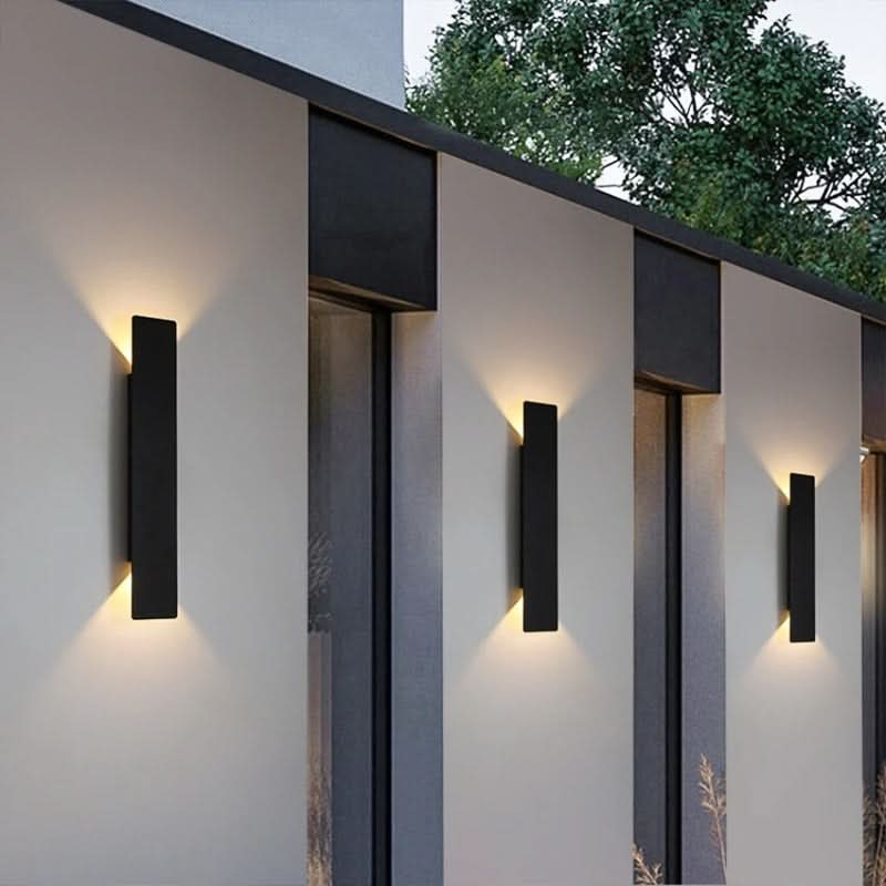 Row of black outdoor wall sconces lighting a modern exterior wall at dusk