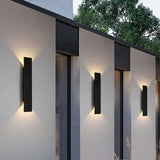 Row of black outdoor wall sconces lighting a modern exterior wall at dusk