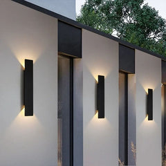 Row of black outdoor wall sconces lighting a modern exterior wall at dusk