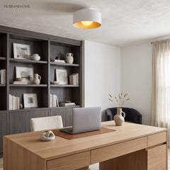 Drum ceiling light with lit wood grain interior above a pale timber desk