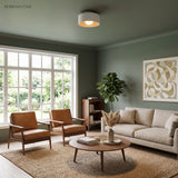 White drum ceiling light lit in a green walled room with leather armchairs
