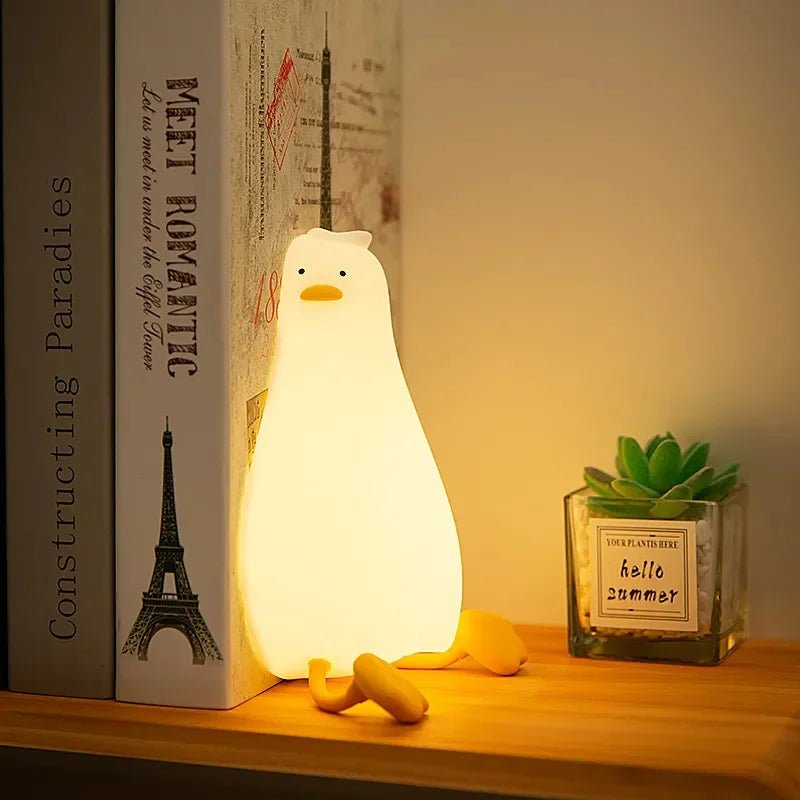 Duck silicone night light glowing warm on a bookshelf beside books and a plant