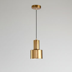 A modern pendant light fixture with a brushed gold finish, featuring a two-tiered cylindrical shade and a thin black hanging cord against a neutral gray background.