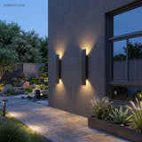 Pair of slim black exterior wall sconces beside a window on a grey facade