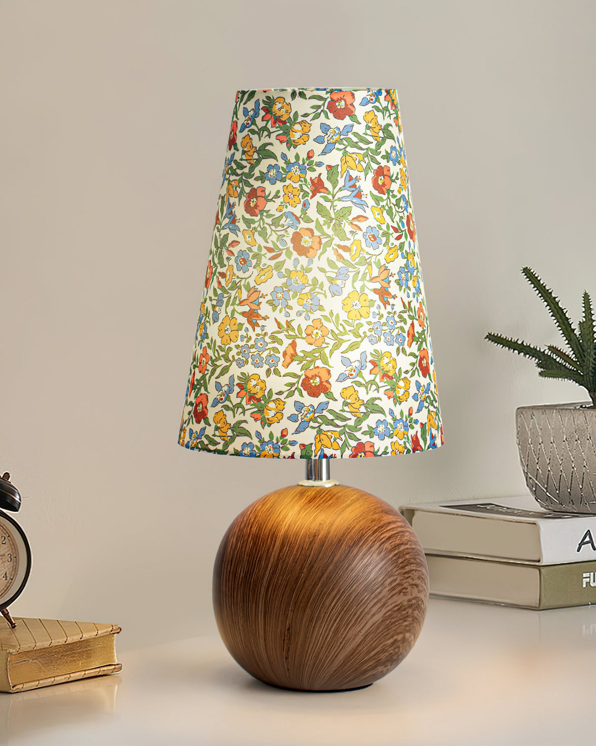 Floral table lamp on a stack of books beside a small potted plant