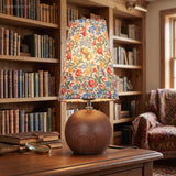 Floral shade table lamp on a dark wood desk in front of full bookshelves