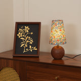 Floral table lamp lit at dusk beside a framed gold botanical drawing