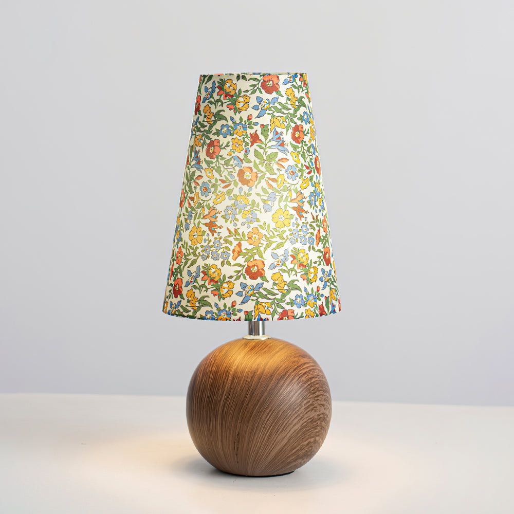 Floral table lamp lit against a plain grey studio background