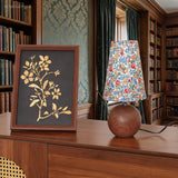 Wood base floral lamp beside a framed botanical print in a panelled library