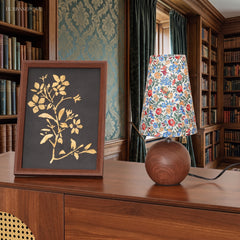 Wood base floral lamp beside a framed botanical print in a panelled library