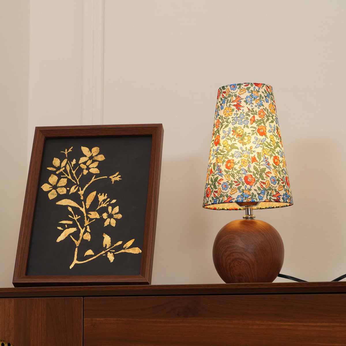 Floral table lamp glowing on a walnut sideboard in a panelled room