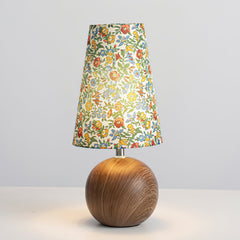Floral table lamp lit on a pale grey background showing the tapered shade