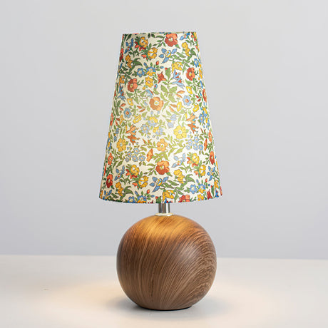 Floral table lamp lit on a pale grey background showing the tapered shade
