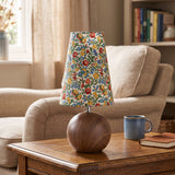 Floral shade table lamp with a round walnut base on a polished wood table